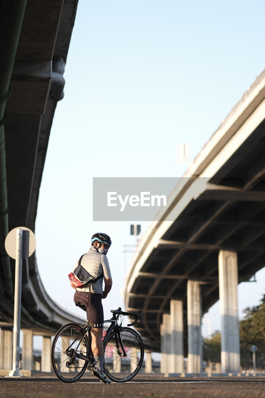 Man riding bicycle under bridge against sky