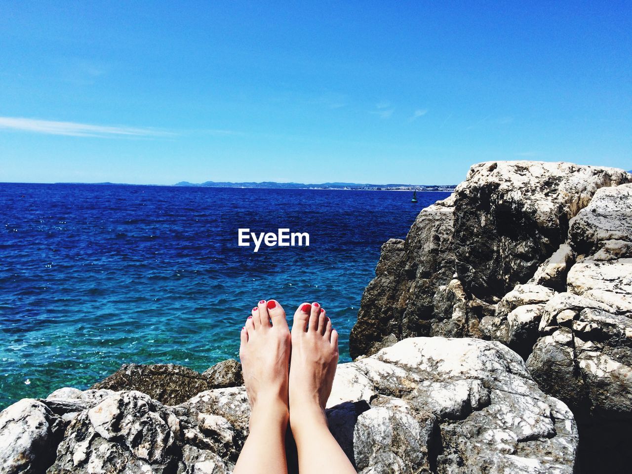 Low section of woman on rocks by sea against sky