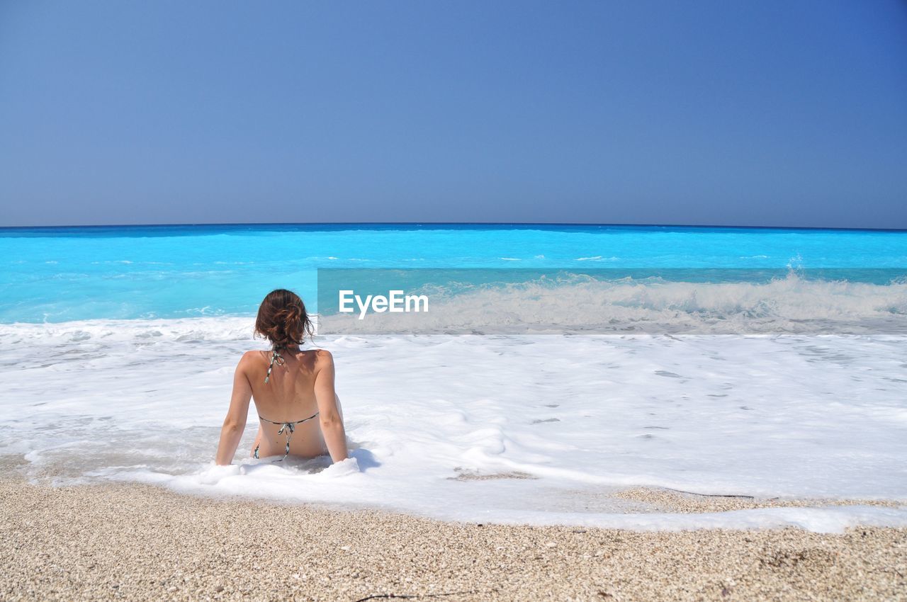Rear view of sensuous woman in bikini relaxing on shore at beach during sunny day