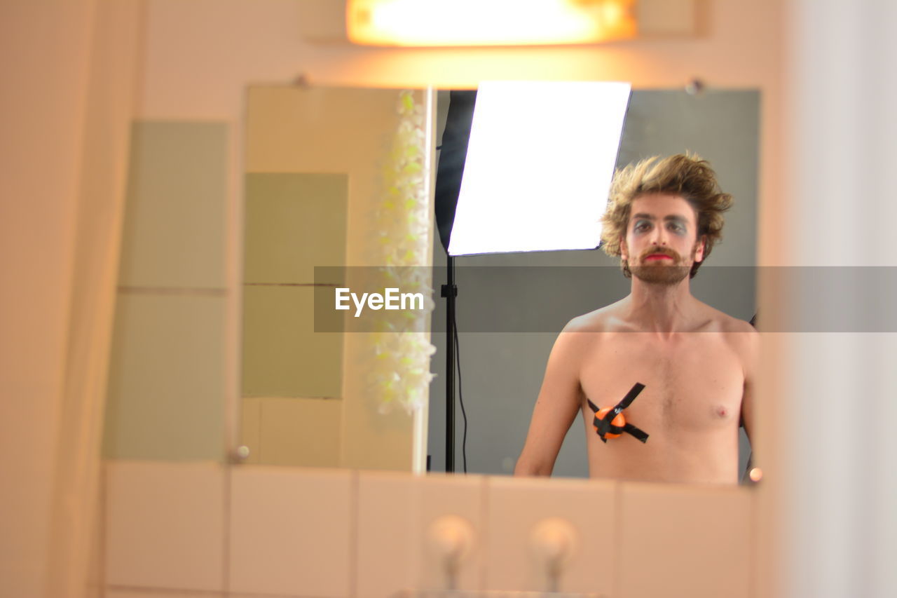 Portrait of shirtless man with face paint and duct tape on chest in bathroom