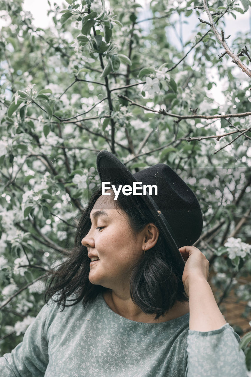 Beautiful asian plus size model wearing green dress enjoying smell of blooming spring tree outdoor