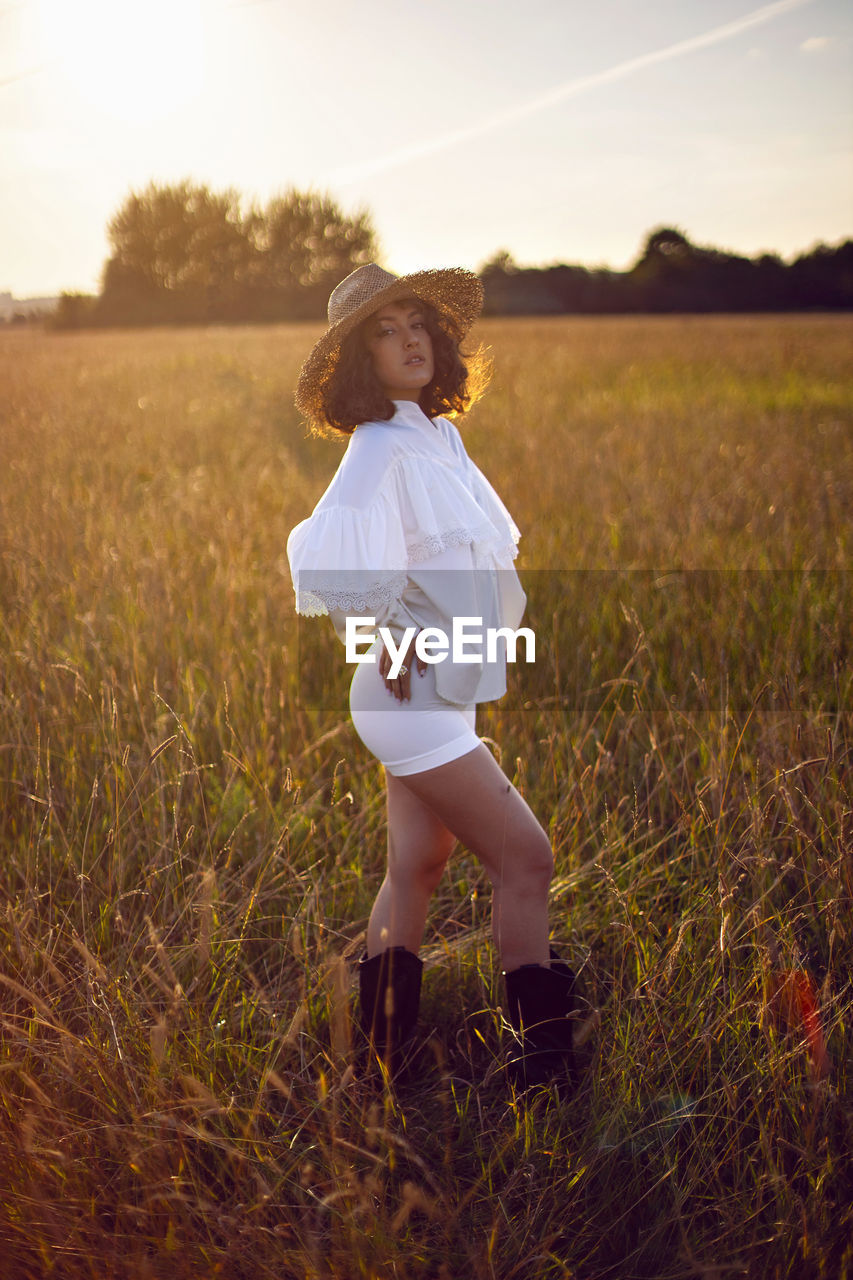 Portrait woman in white clothes and in a wicker hat stand on a field with grass in autumn