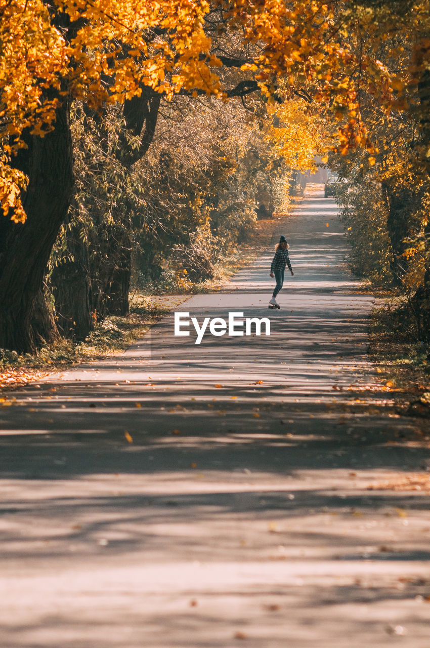 Man walking on road amidst trees during autumn