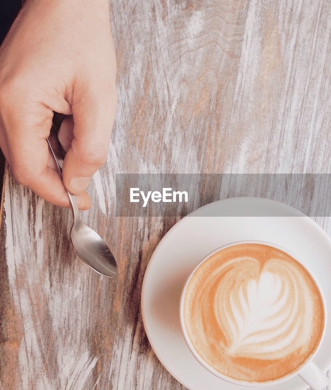 Cropped image of person holding spoon while having coffee on table