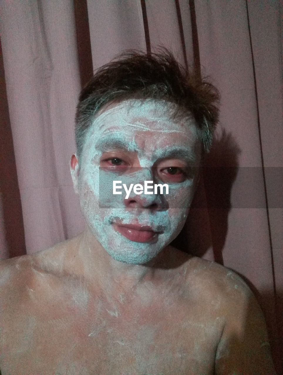 Portrait of young man with face mask against curtain