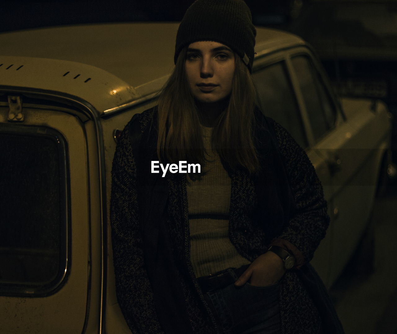 Portrait of young woman leaning on car at night