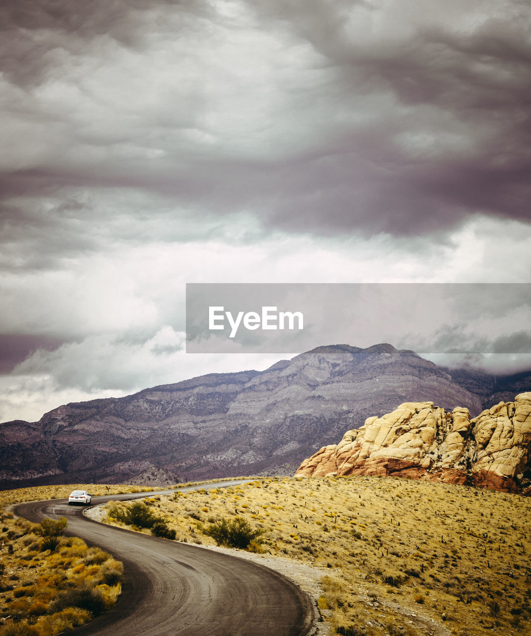 Road leading towards mountains against cloudy sky