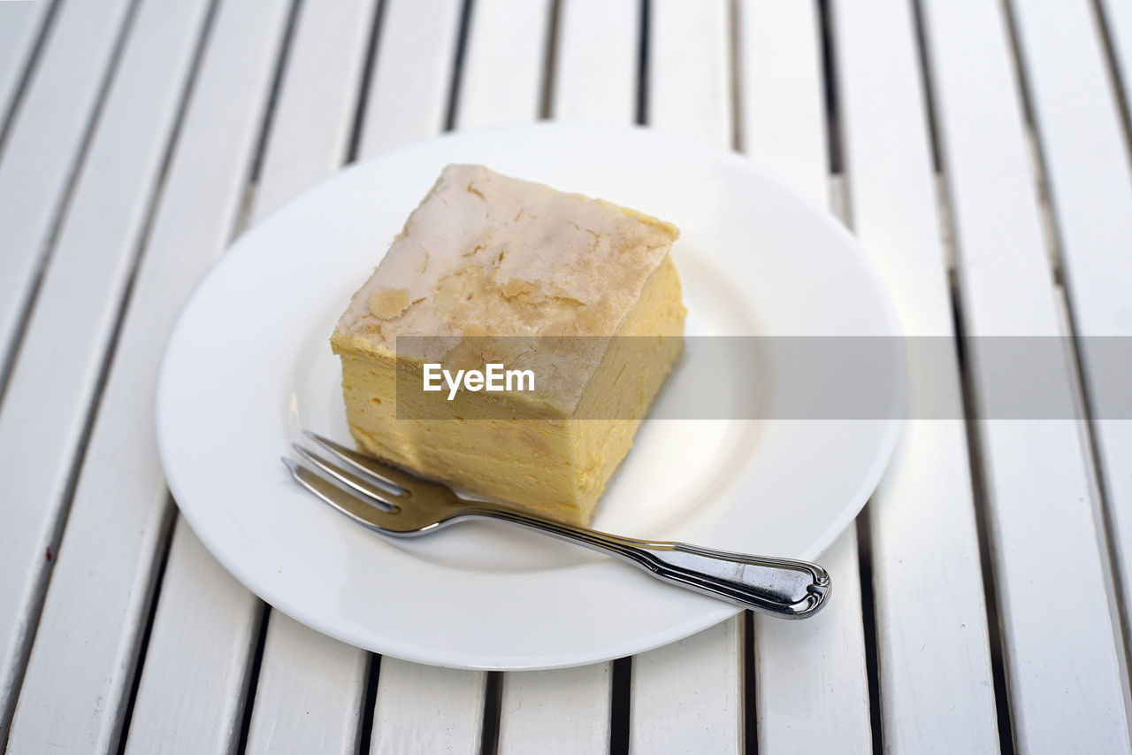 Piece of vanilla custard cream cake with fork on the plate on the table