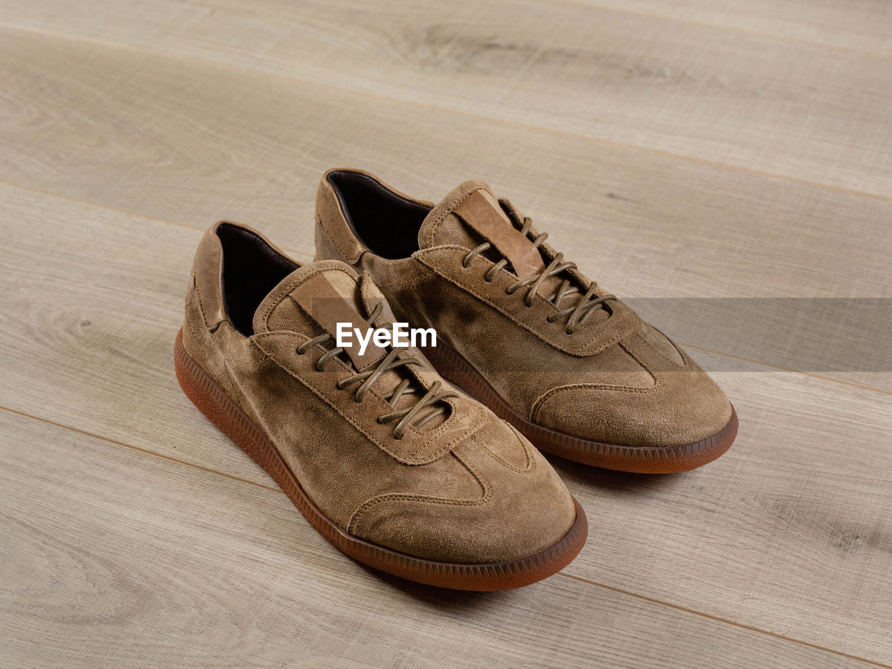 Soft light brown men's shoes for sports lying on a surface of light boards, close-up