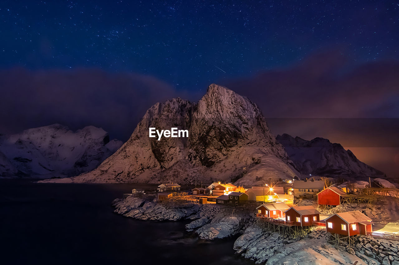 Illuminated building by mountains against sky at night