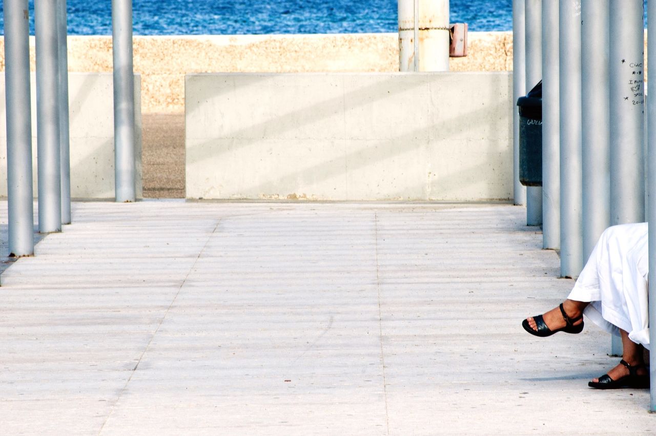 Low section of woman sitting by poles on beach