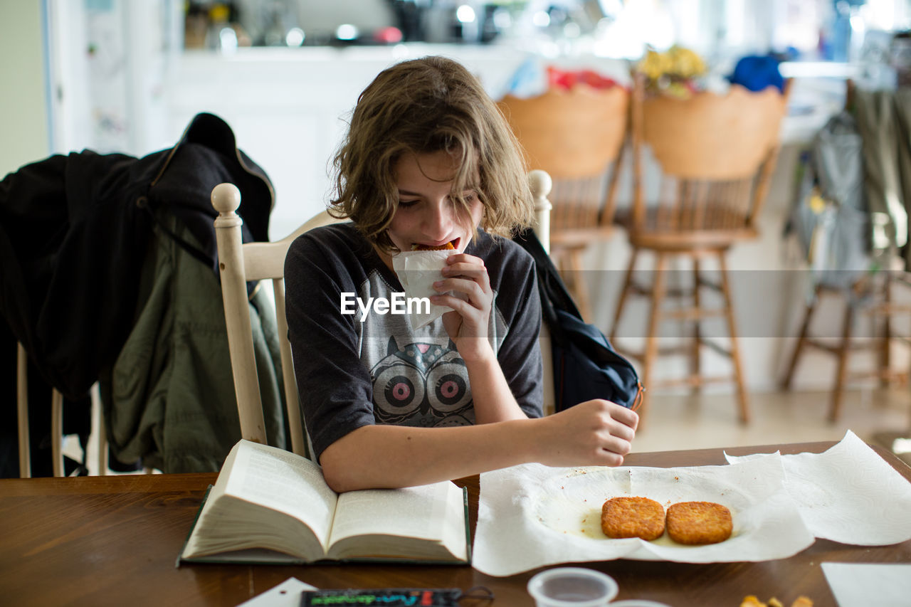 Teen girl takes a bite of a hash brown while she reads her book