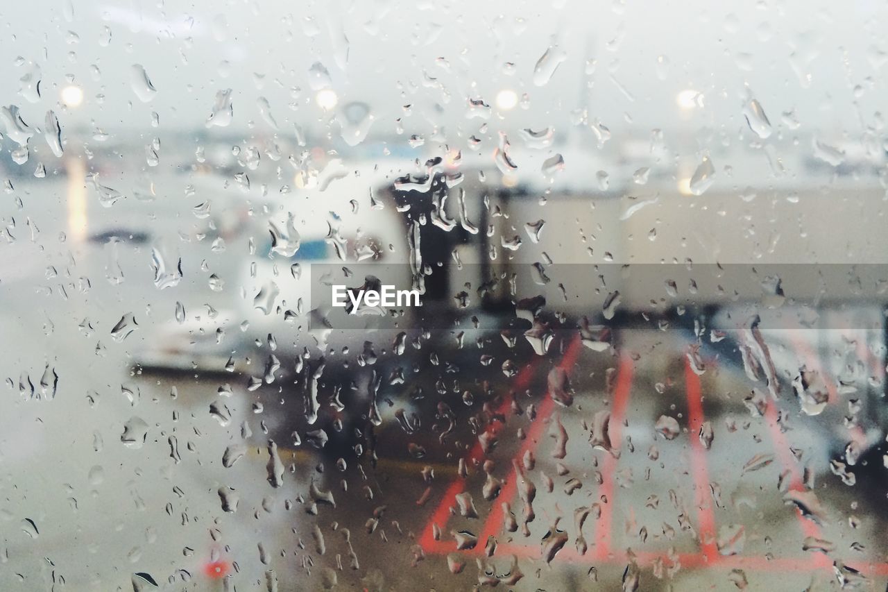 Full frame shot of wet window glass against airplane on runway at airport