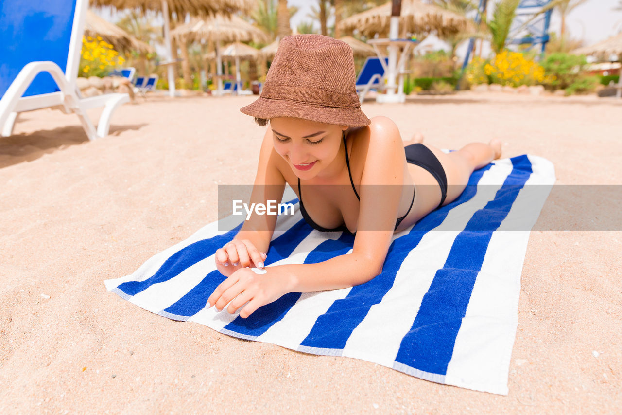 Happy woman applying sunscreen while lying on towel at beach