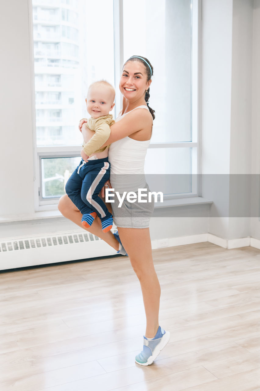 Full length of mother with son exercising on hardwood floor