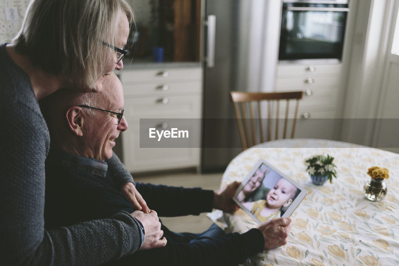 Smiling couple having video chat with baby grandson on tablet