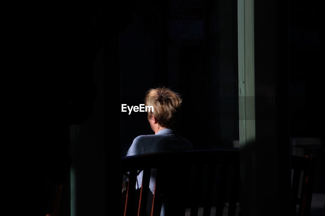 Rear view of woman sitting on bench in darkroom