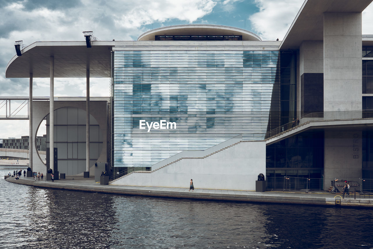 Buildings by river in city against cloudy sky 