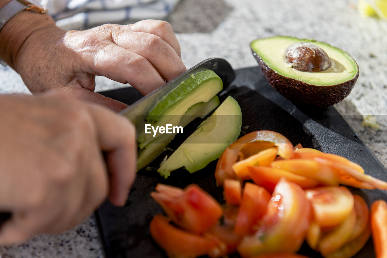 Close up of old lady hands chopping avocados and tomatoes.