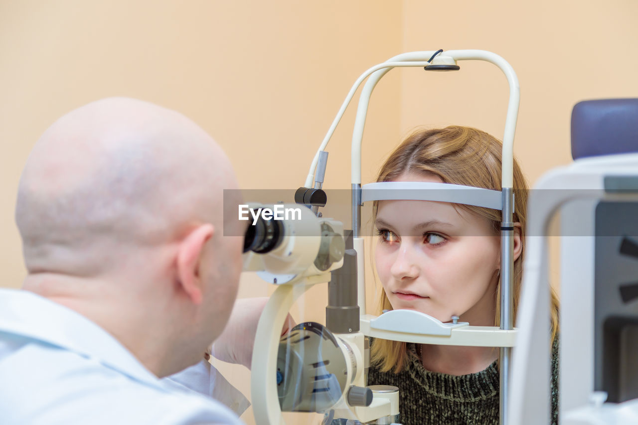 A male ophthalmologist checks the eyesight of a young girl using a modern device with a light beam