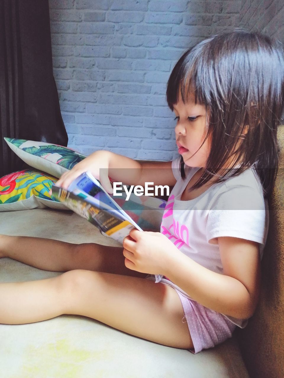 Girl holding book while sitting on sofa at home