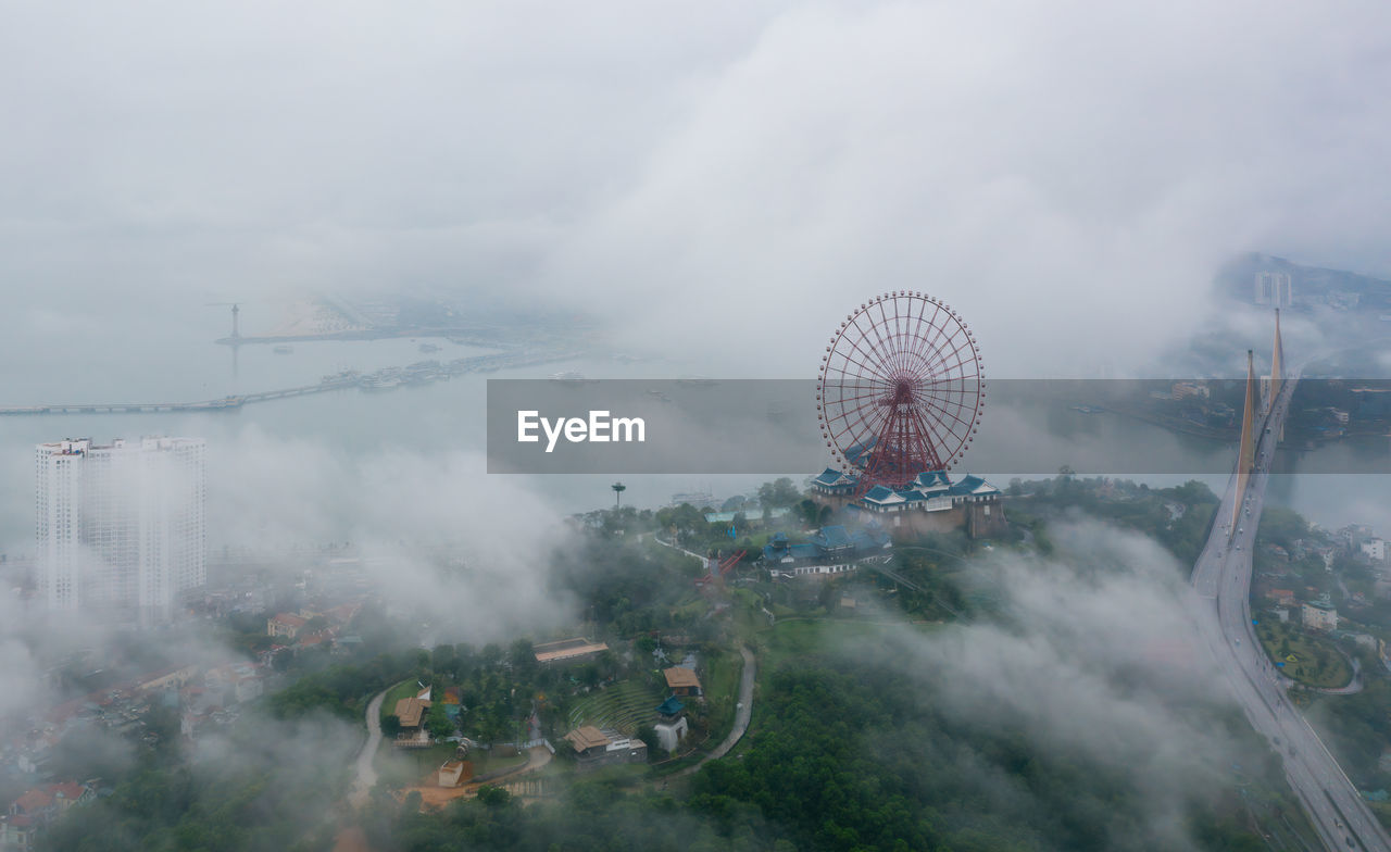 Aerial view of ferris wheel and bridge in city during foggy weather