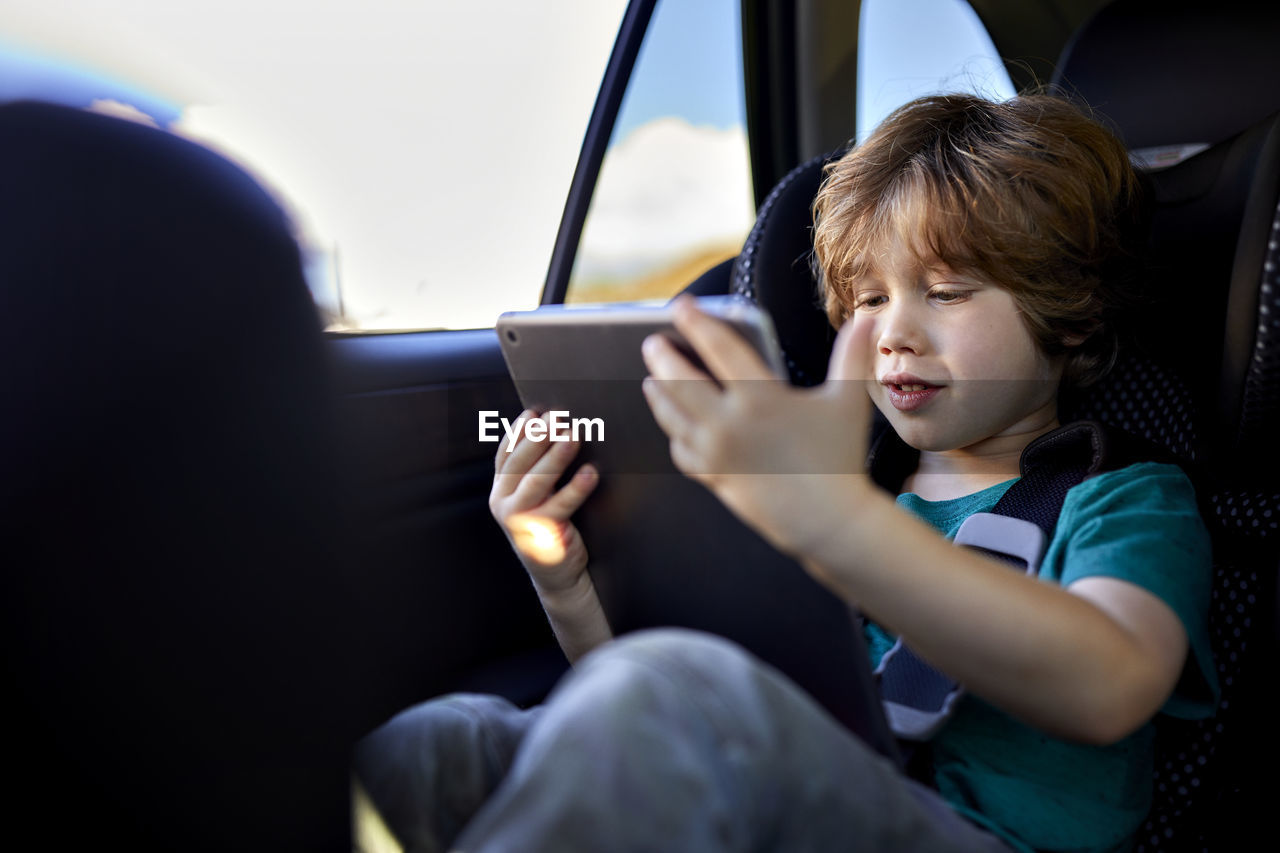 Cute boy using digital tablet while traveling in car during weekend