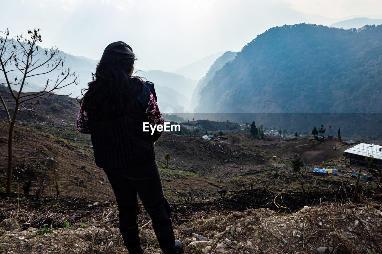 Young girl watching the misty mountain valley with sun rays beams at morning from flat angle