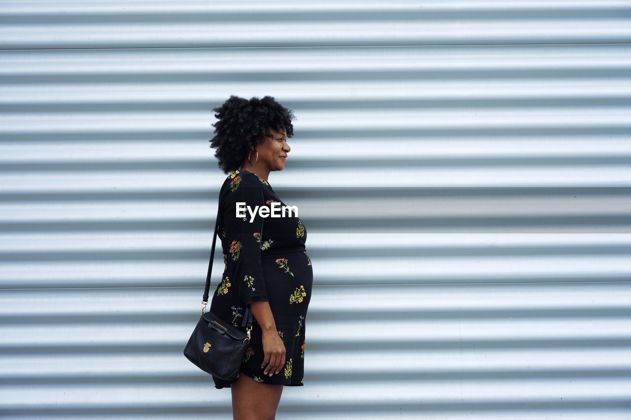 Side view of mid adult woman with shoulder bag standing against wall