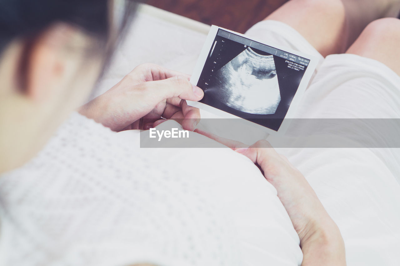 MIDSECTION OF WOMAN HOLDING MOBILE PHONE WHILE LYING ON BED