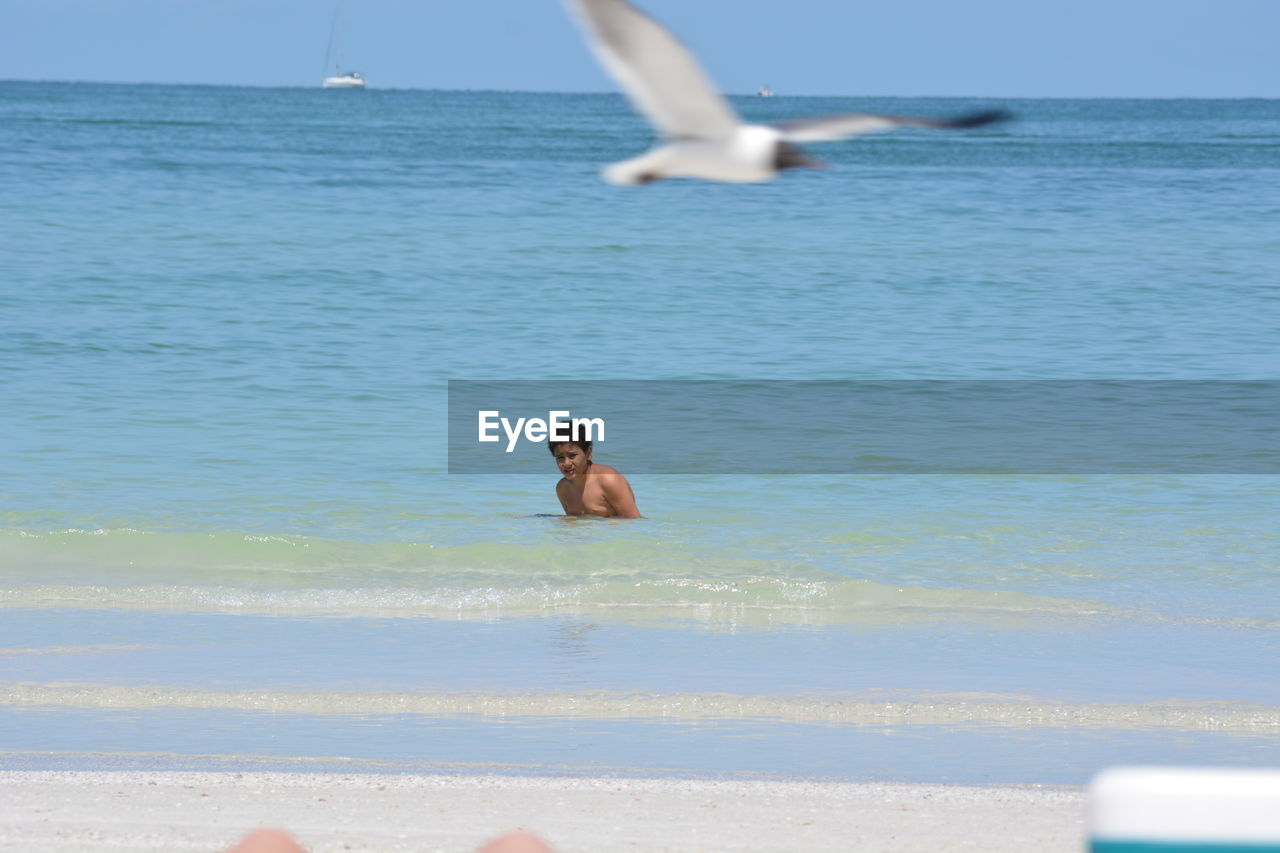 SHIRTLESS BOY IN SEA AGAINST SKY