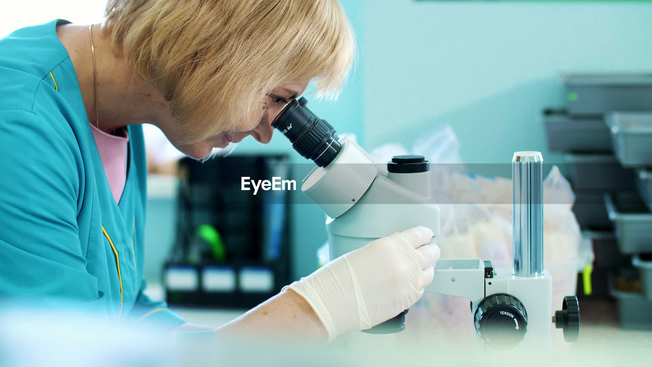 Portrait of lab worker, biochemist in white gloves, studying, examines something with microscope