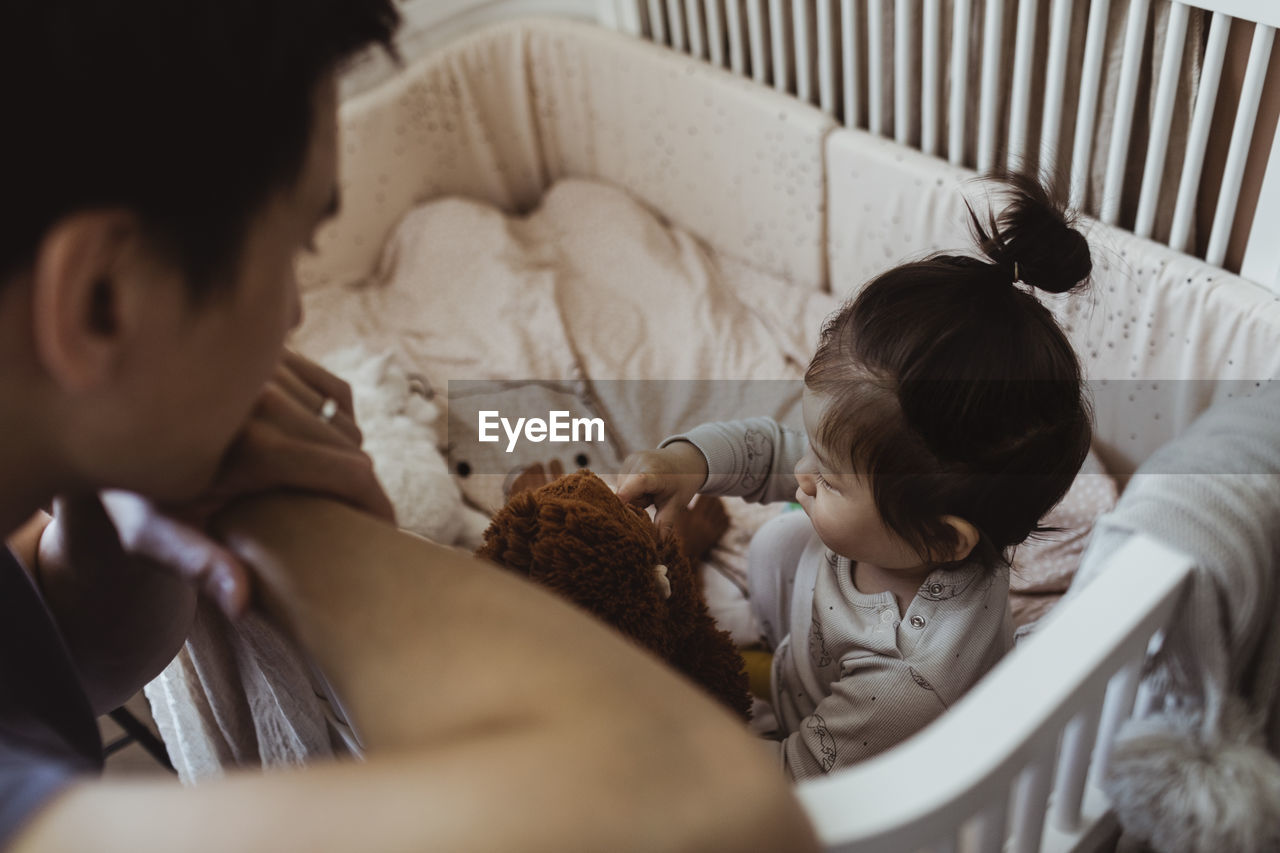 Father looking at baby son playing in crib at home