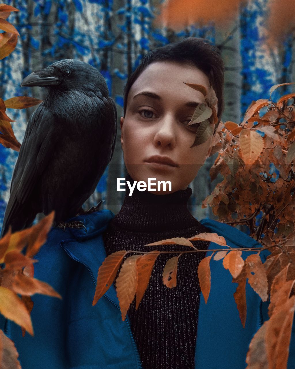Portrait of woman with raven perching on shoulder in forest