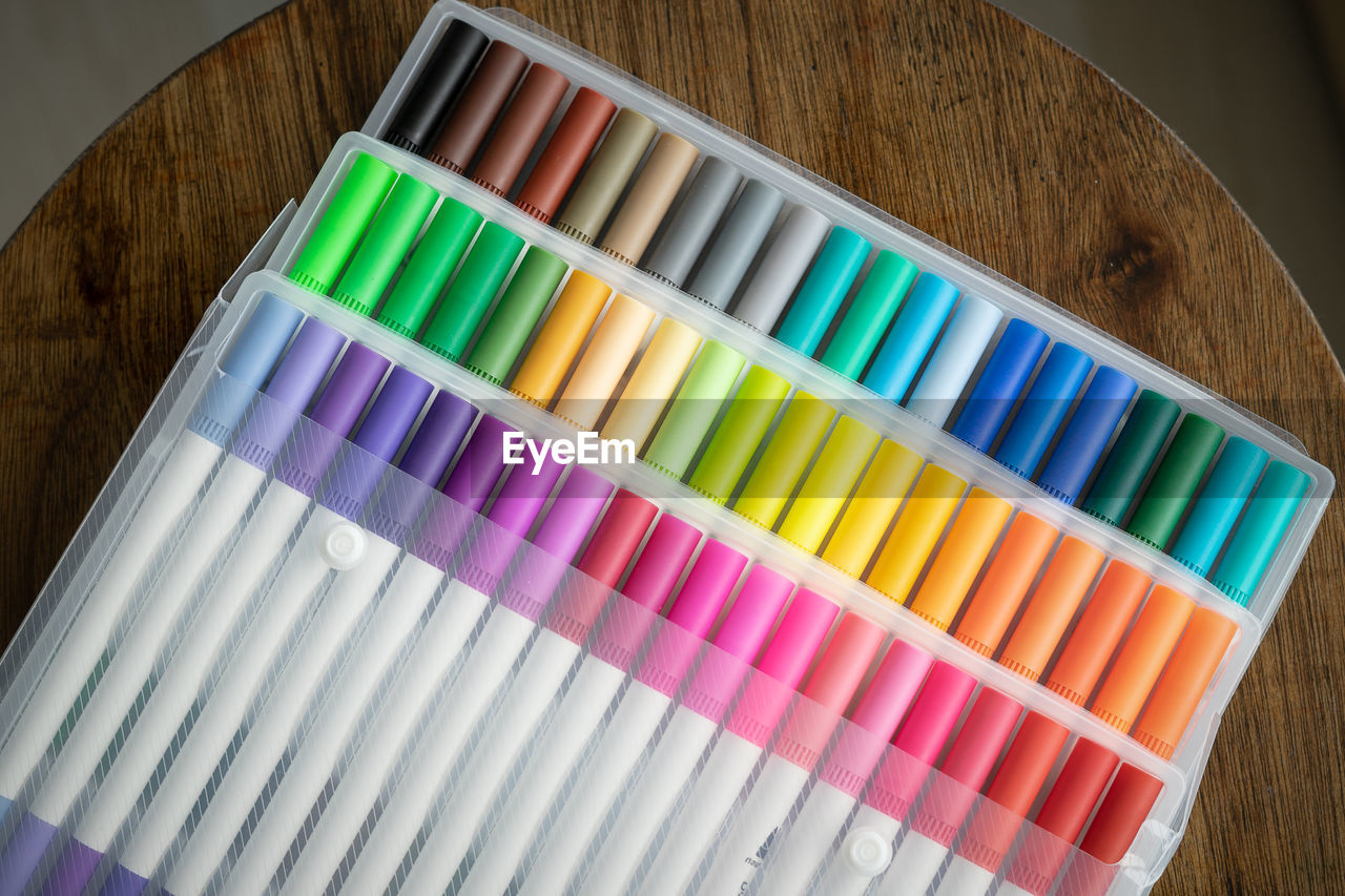 60 pieces of colorful markers in transparent plastic packaging on a wooden background.