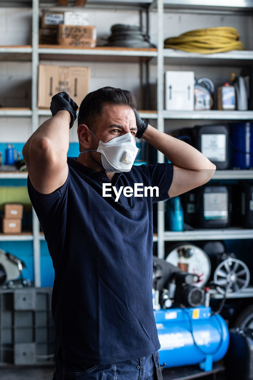 Male employee putting white face mask for work in garage