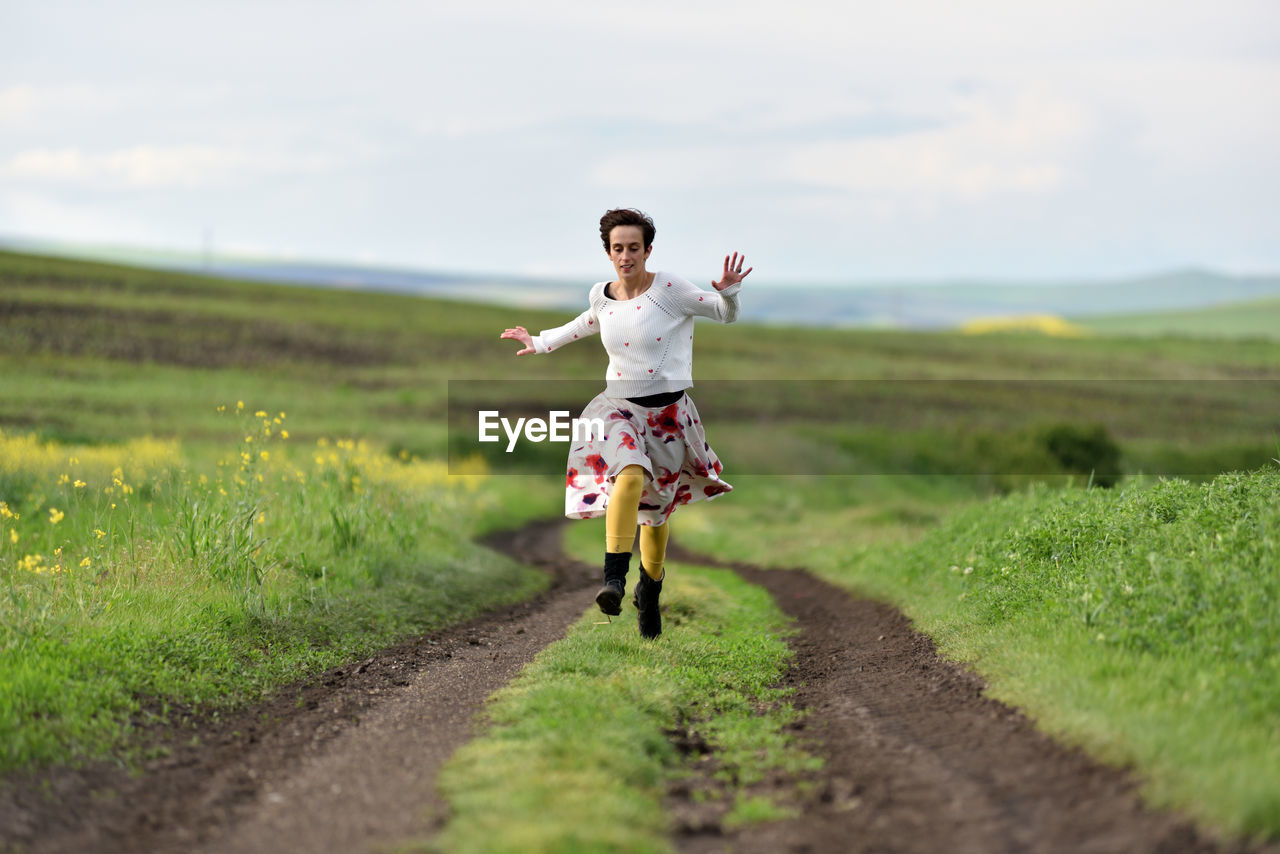 Full length of young woman running on road over field