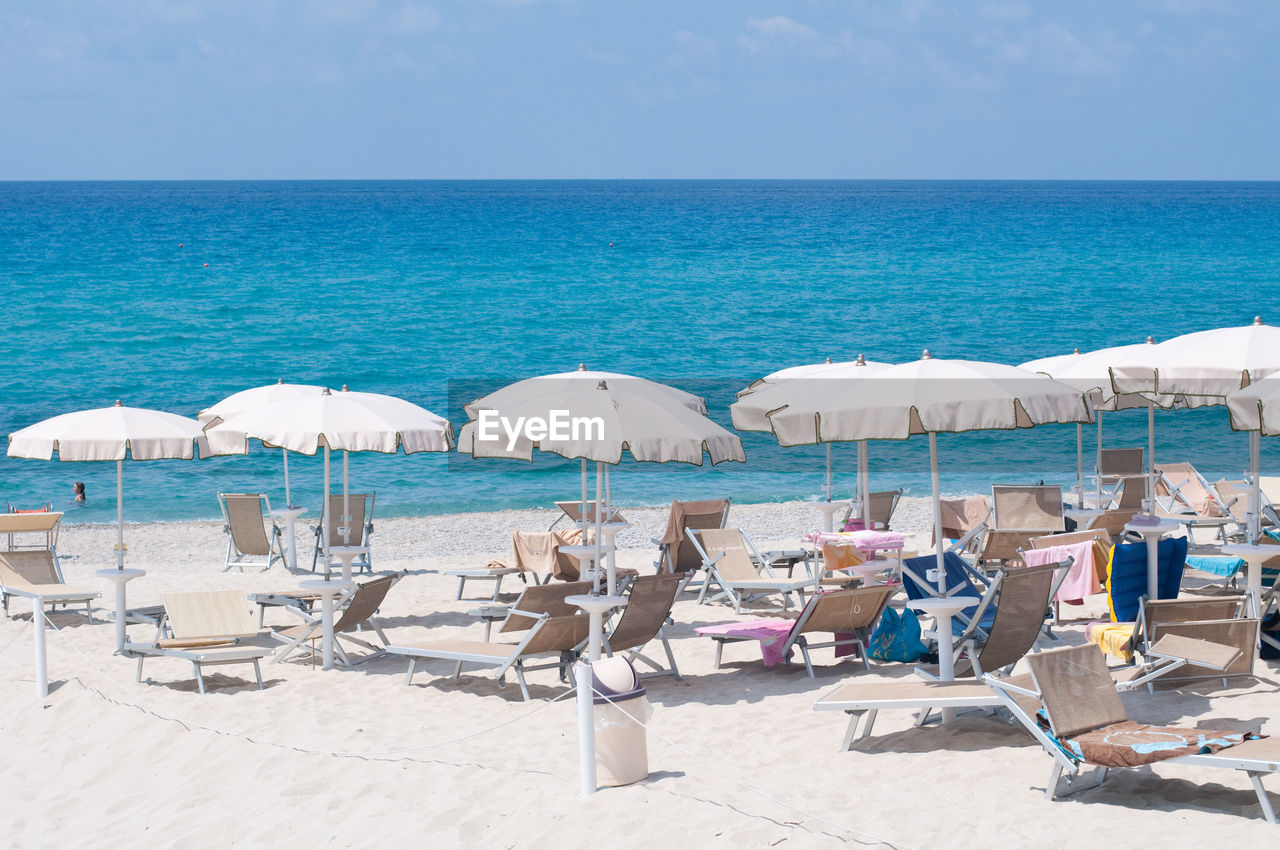 LOUNGE CHAIRS ON BEACH AGAINST SKY