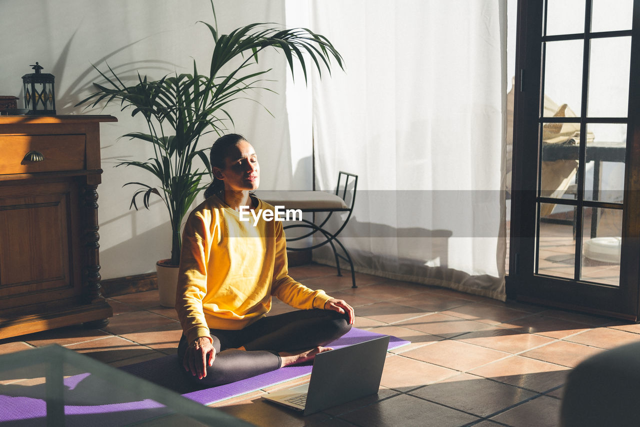 Young caucasian brunette woman practicing yoga at home sitting in lotus pose.