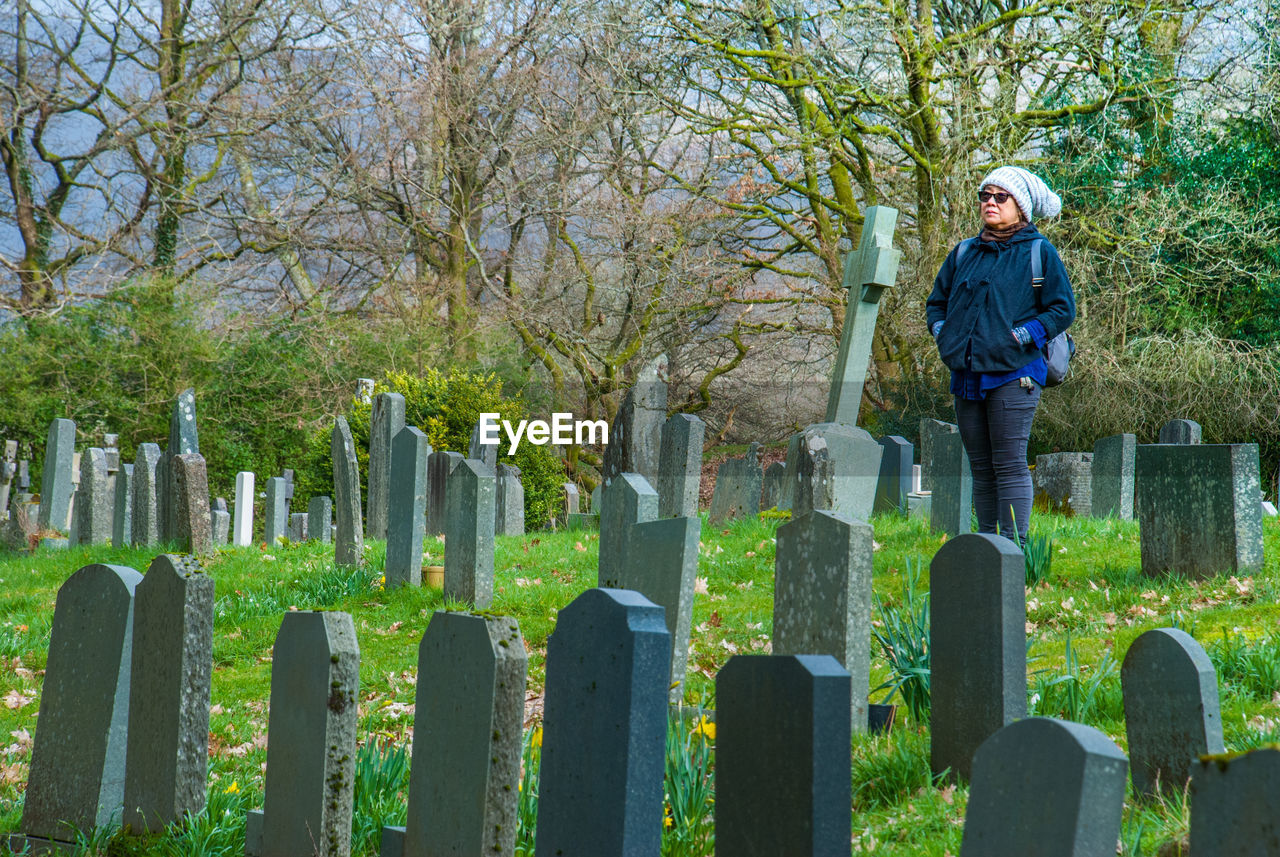 Woman with hands in pockets standing in grave yard