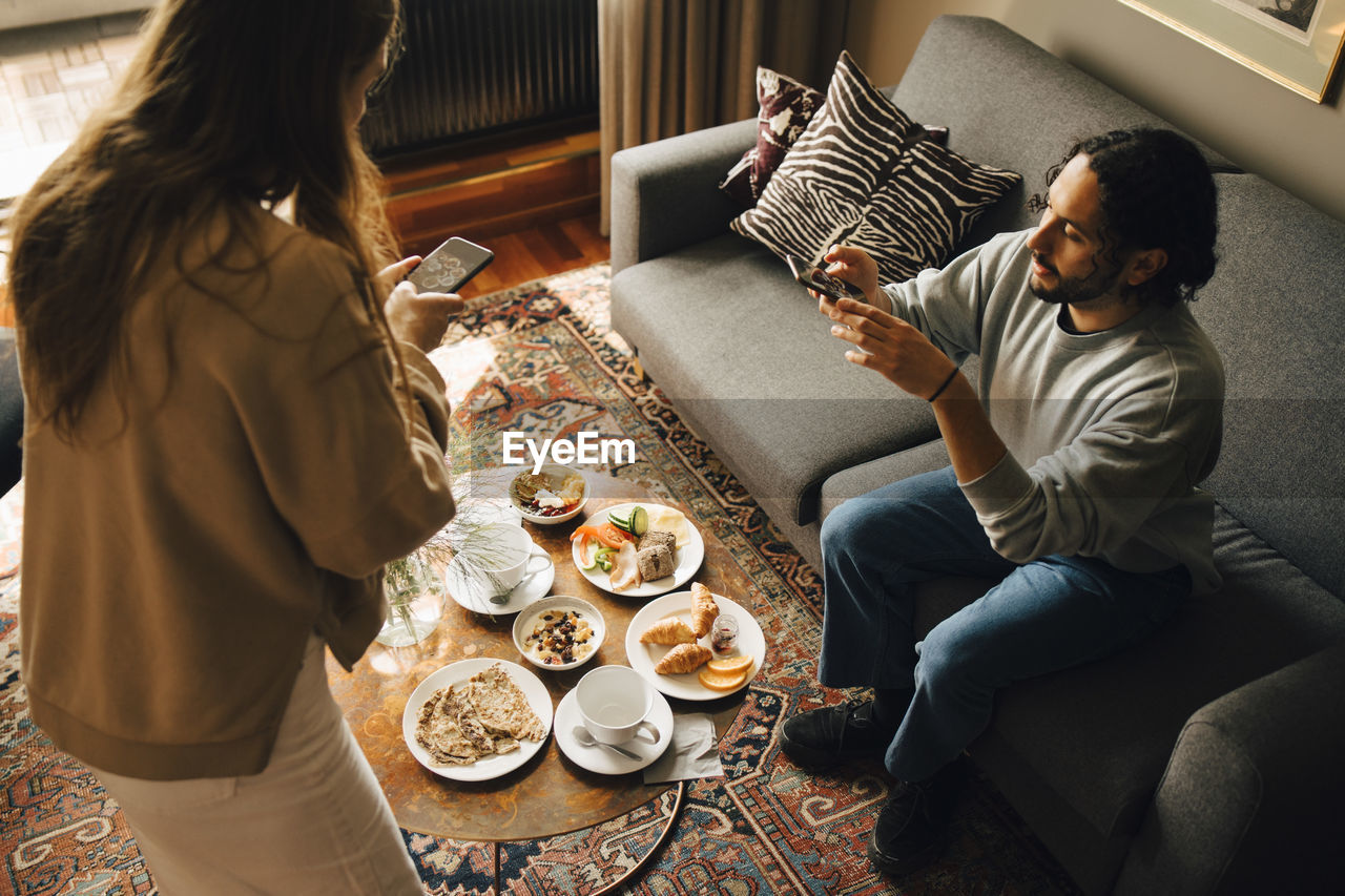 High angle view of couple photographing breakfast in hotel room