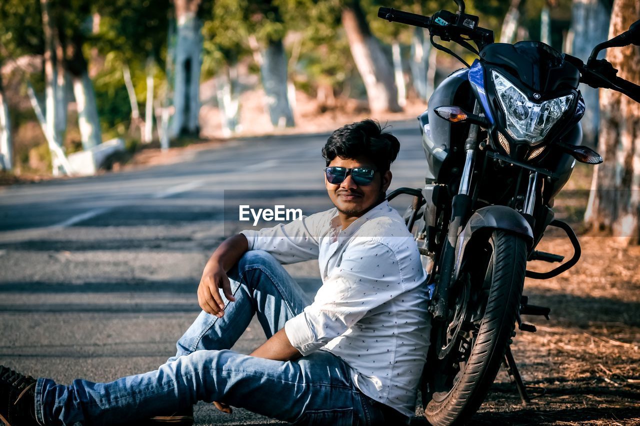 Portrait of young man wearing sunglasses while sitting by motorcycle on road