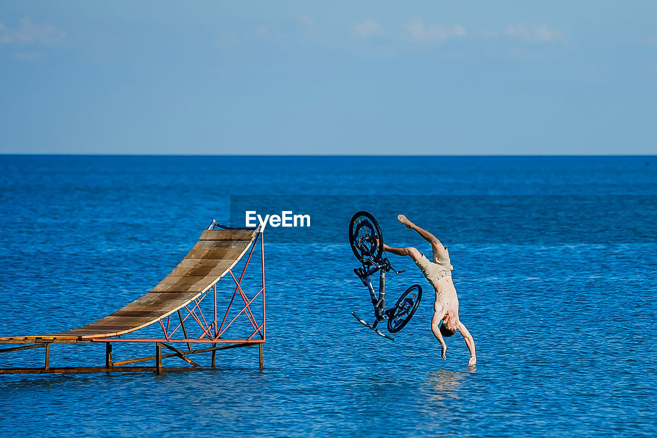 Full length of young man with bicycle diving in sea against sky