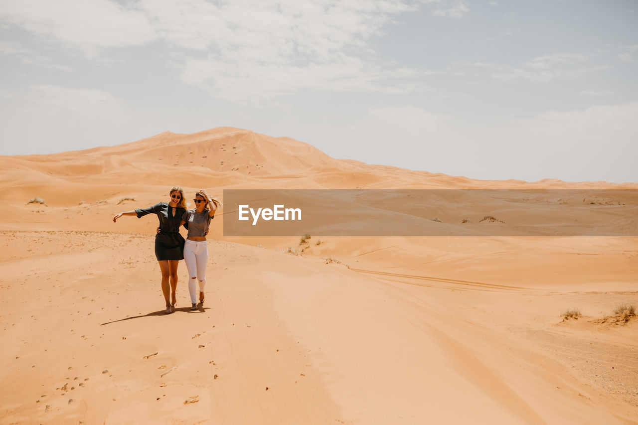 Smiling young friends walking at desert against sky