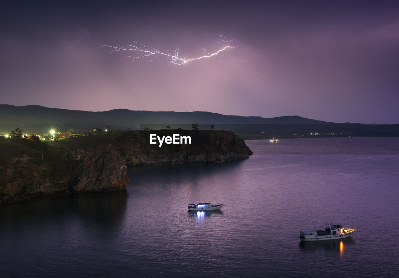 Boats sailing in sea during lightning in sky at dusk