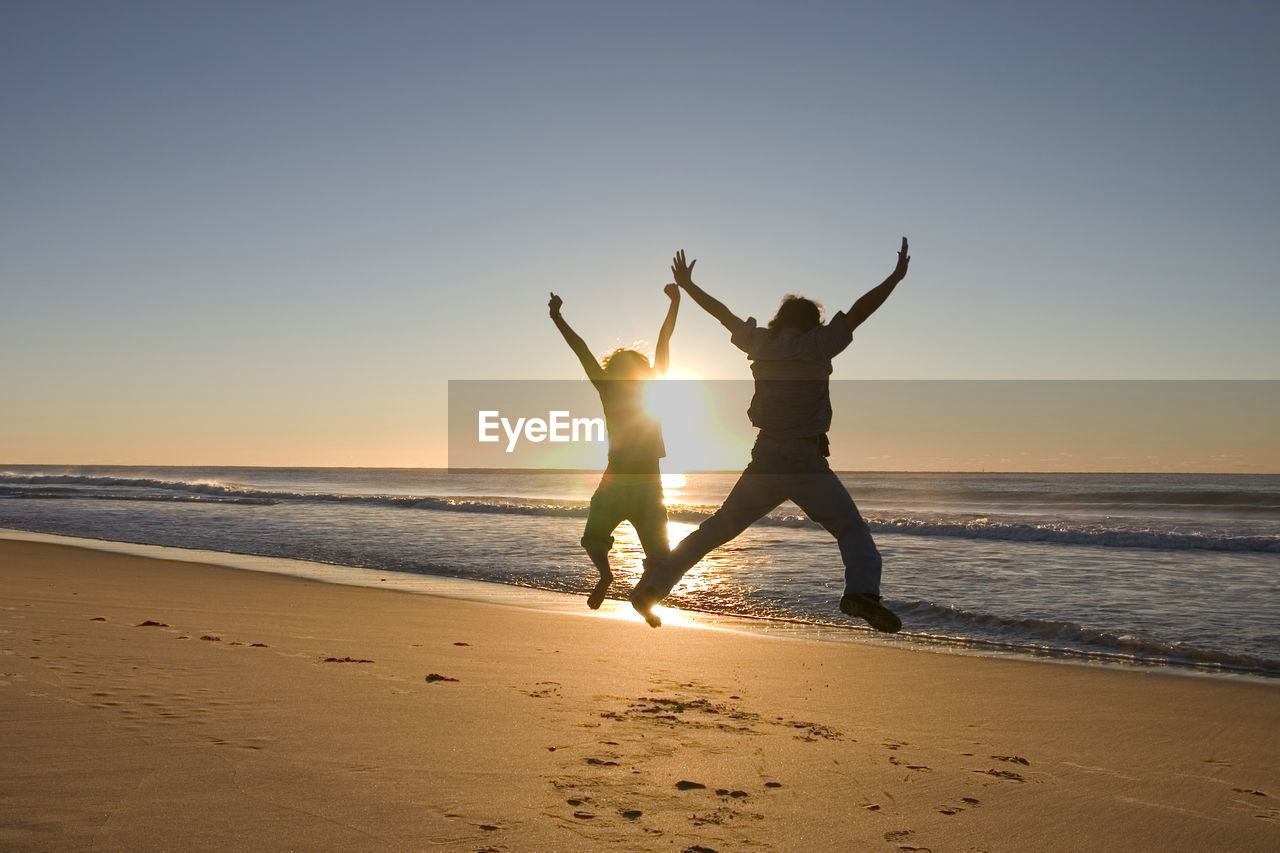 Silhouette people jumping at beach against sky during sunset