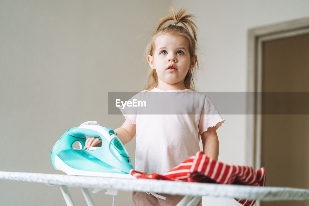 Cute little baby girl playing and ironing clothes with an iron at home