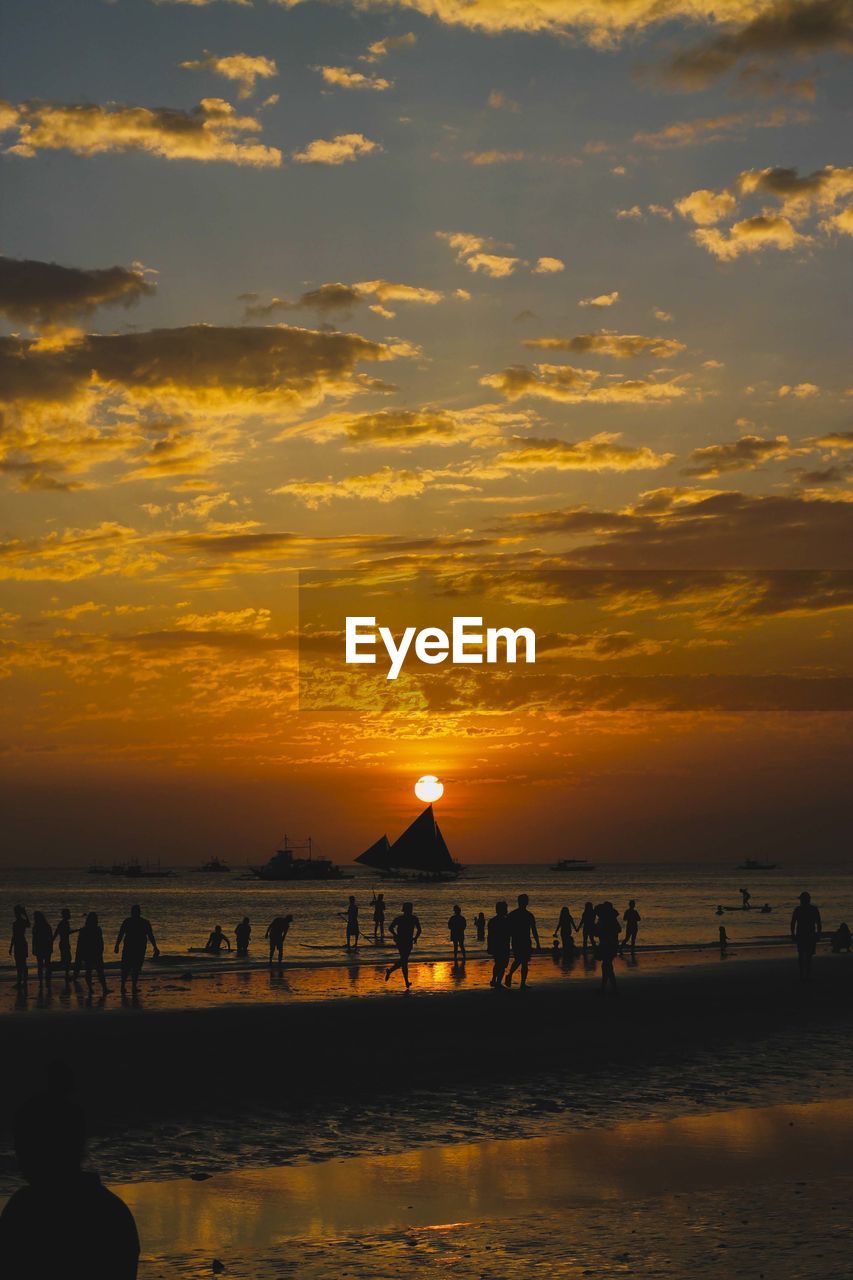 Silhouette people at beach against sky during sunset