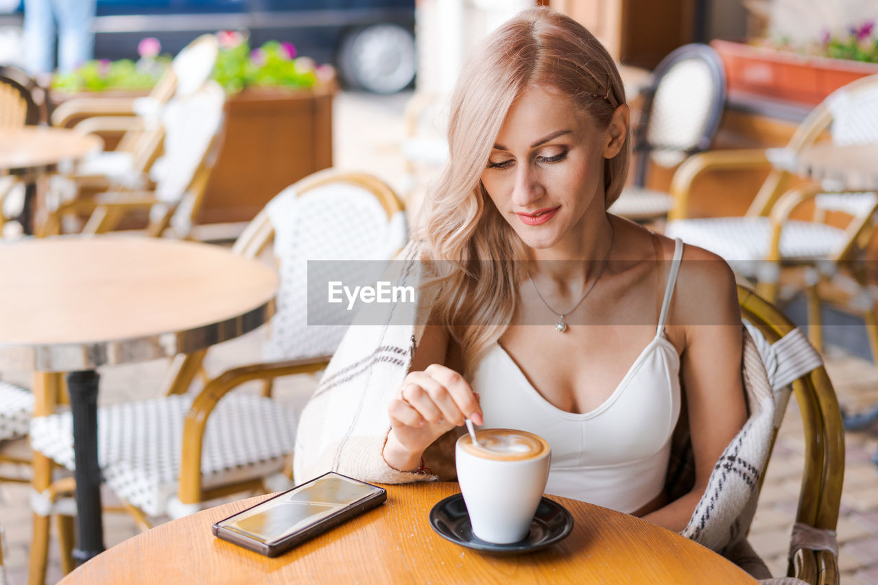 Young woman while relaxing in cafe at table on street, happy caucasian woman