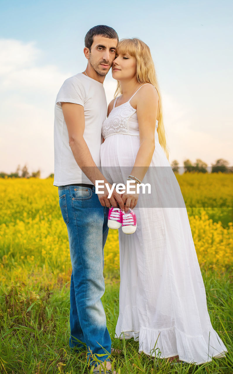 Portrait of couple holding baby shoes while standing on field